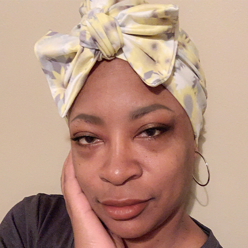 Jenita Stubblefield poses with her hand on her face and wearing a head wrap.