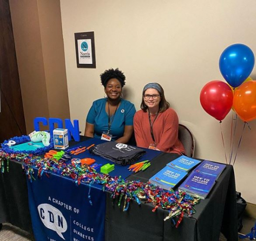 Quisha Umemba, MPH, BSN, RN, CDCES, CHWI and Kacey Creel smile while working at a College Diabetes Network table.